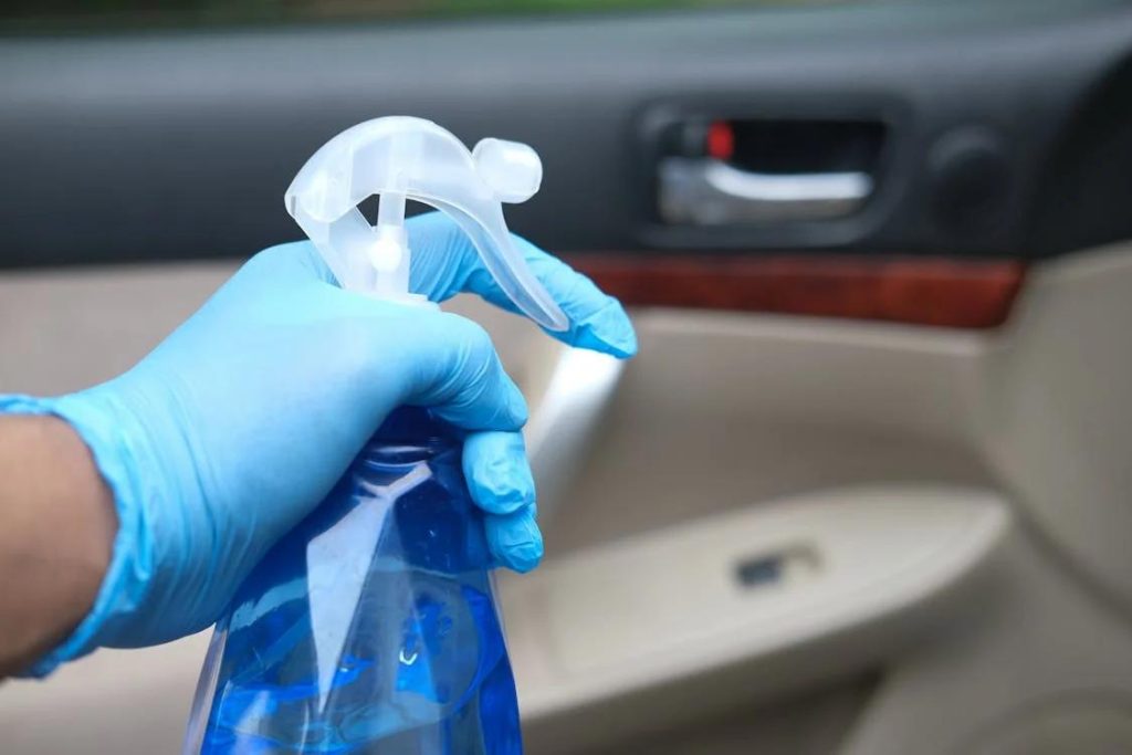 Interior detailing services provider holding a spray bottle with a car’s interior in the background 