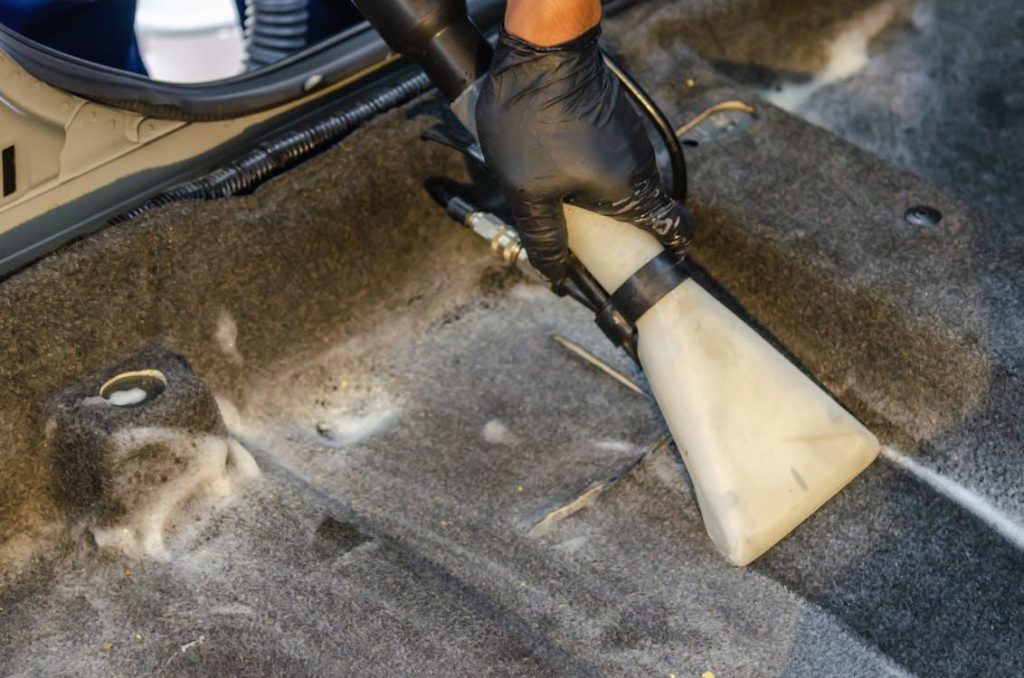 Interior detailing services provider cleaning a car’s mat with a vacuum 