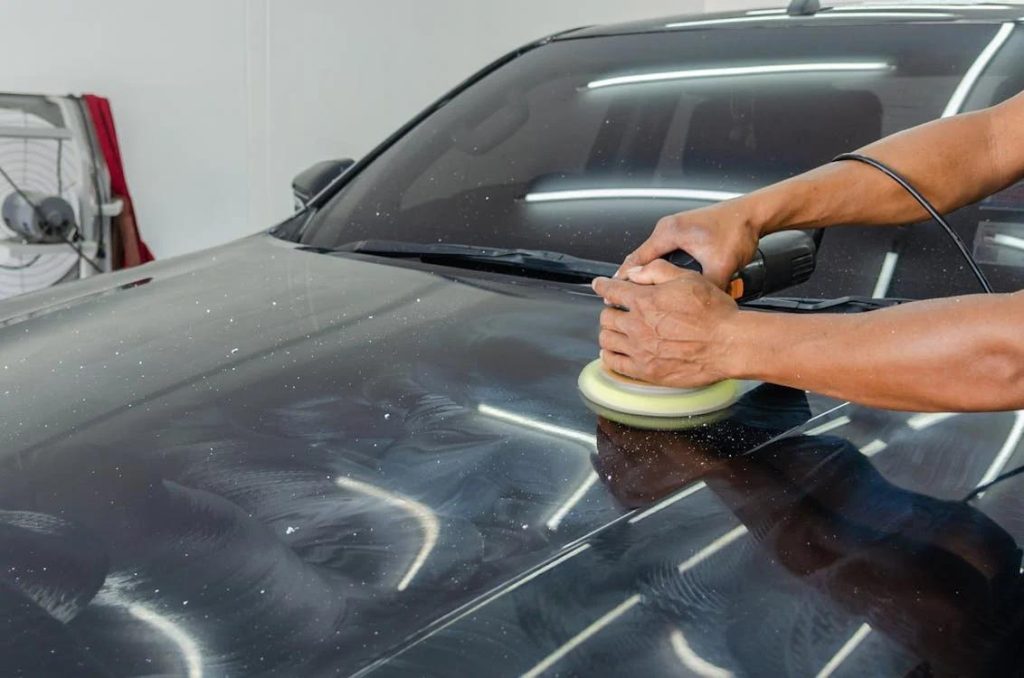 A professional car polishing expert using a polishing machine on a black car
