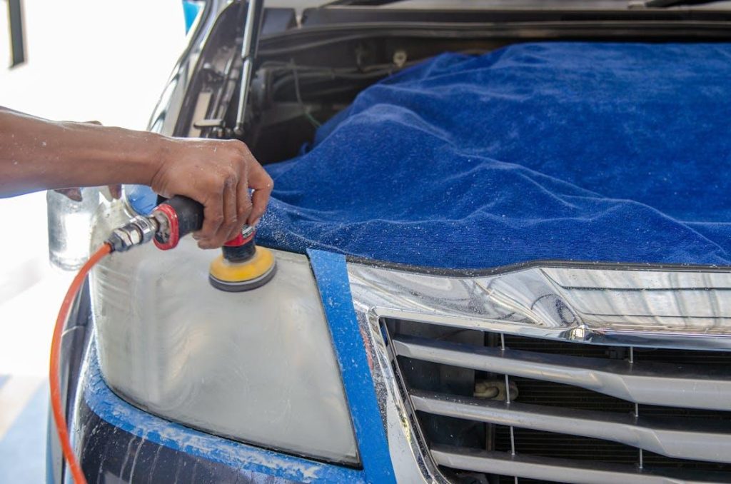 A professional car polishing expert using a polishing machine on a car covered by a blue cloth