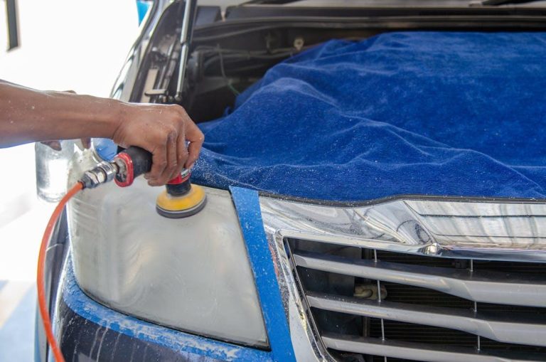 A professional car polishing expert using a polishing machine on a car covered by a blue cloth