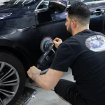 Auto detailer using a machine polisher on the side of a dark Volkswagen during paint correction