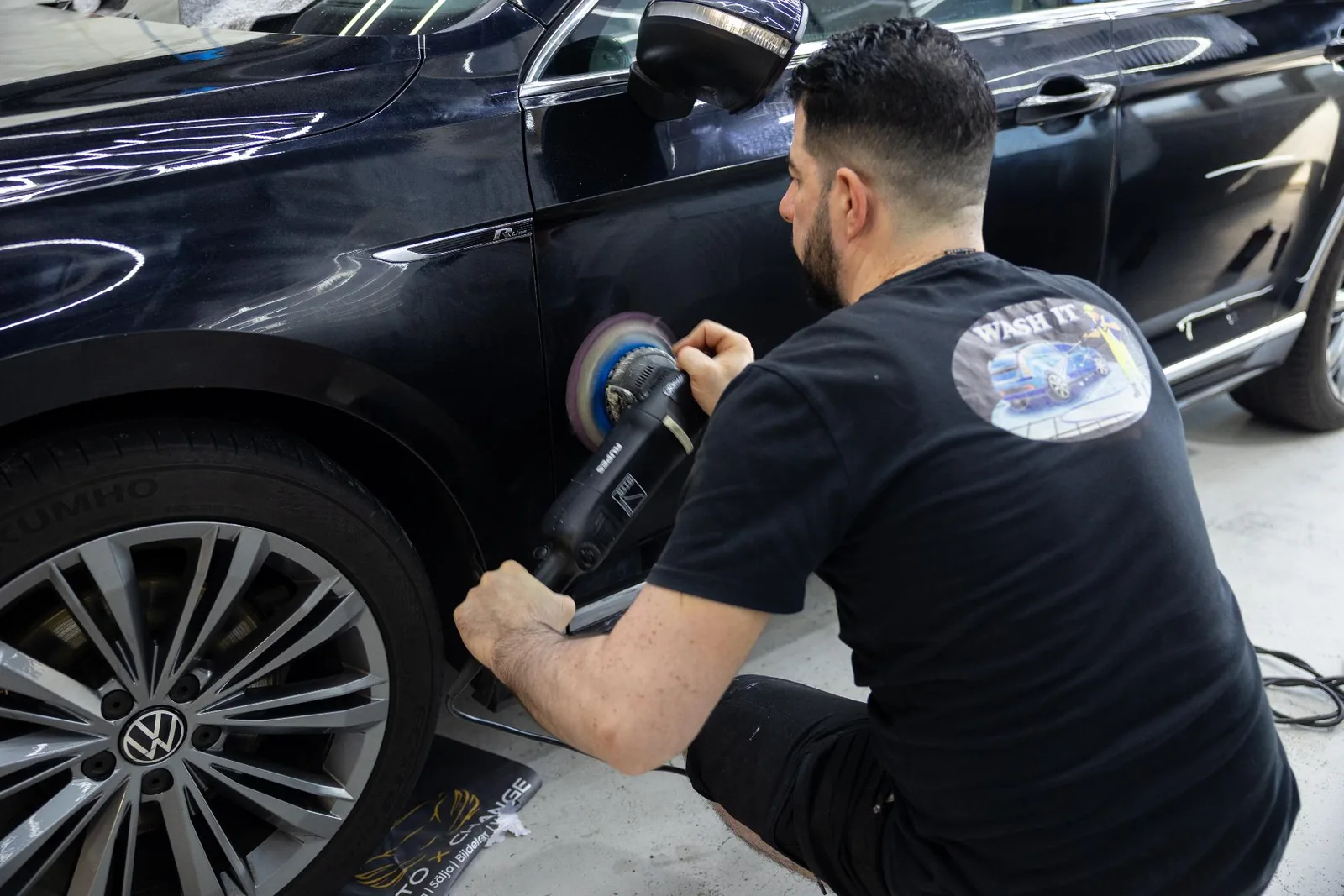 Auto detailer using a machine polisher on the side of a dark Volkswagen during paint correction